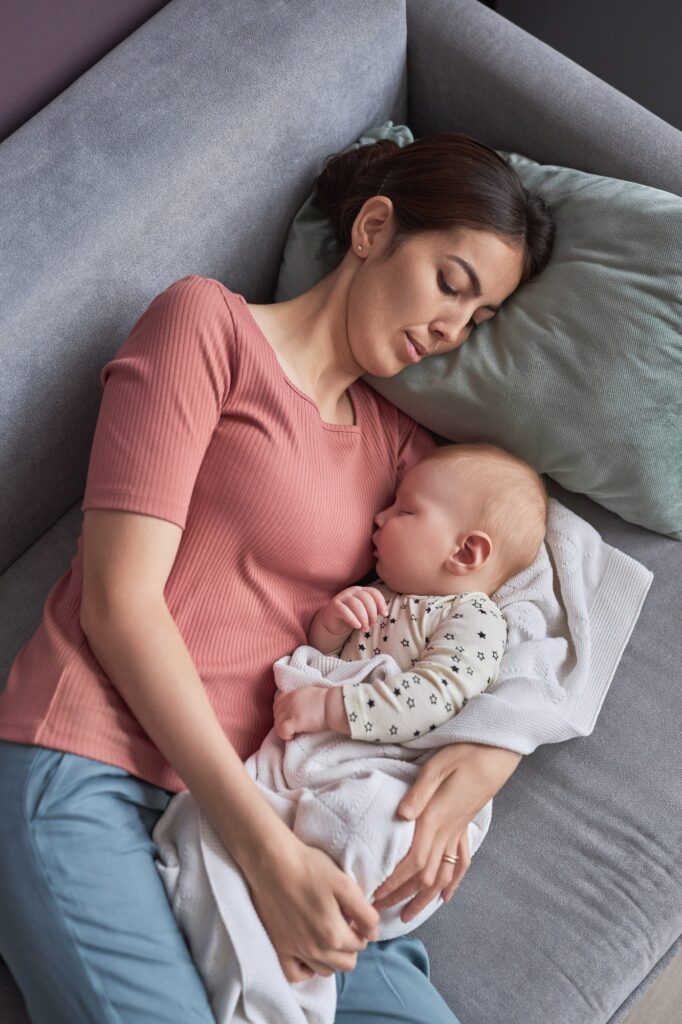 Tired Young Woman Sleeping with Little Baby on Couch During Naptime